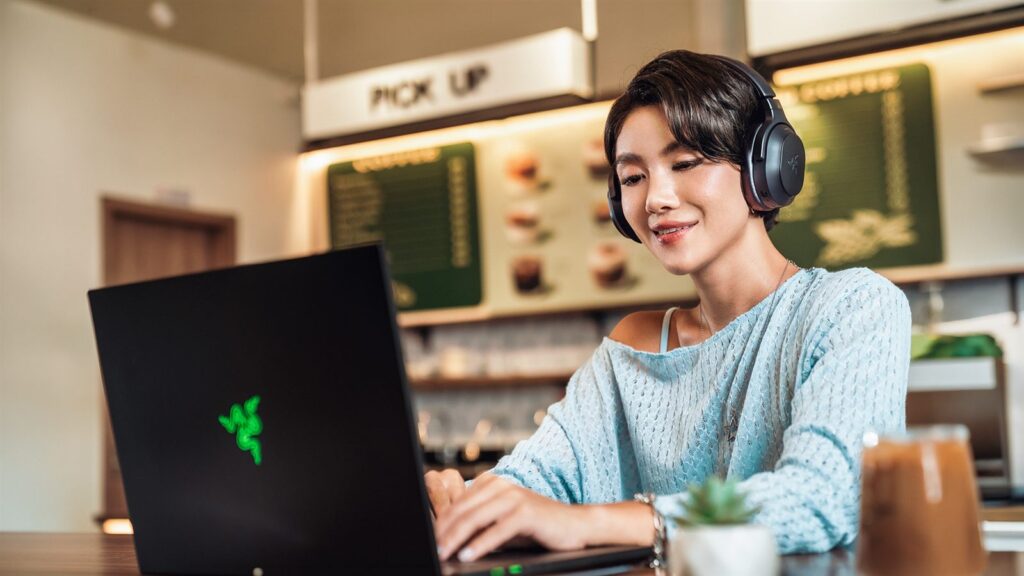 Razer Barracuda V2 Pro: headset sem fio tem ANC híbrido, THX Spatial Audio+ e 70 horas de bateria Mulher usando o headset Razer Barracuda V2 Pro sem o microfone boom enquanto trabalha no notebook em um café